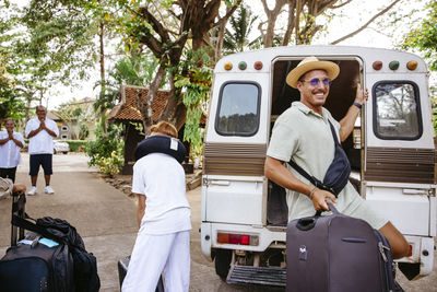 Smiling male tourist getting down with luggage from van at resort during vacation