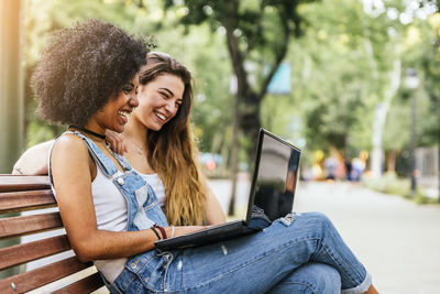 Young woman using phone while sitting on bench