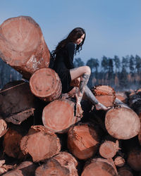 Side view of woman sitting on logs against clear sky