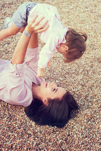 Mother playing with daughter while lying down on pebbles
