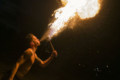 Low angle view of shirtless man spitfire at night