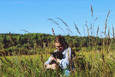 Young woman with dog sitting on grassy field against clear blue sky during sunny day