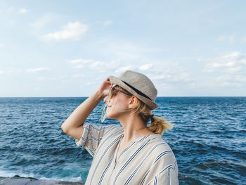 Young woman wearing hat while standing at beach against sky