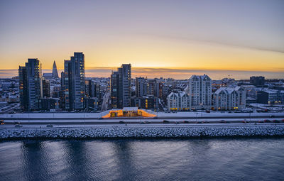 River by buildings against sky during sunset in city