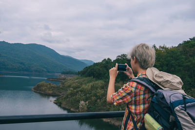 Man photographing on mountain by lake against sky