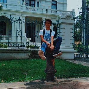 Full length of young man sitting on fire hydrant against house