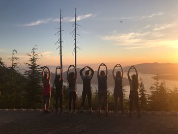Rear view of people with arms raised making heart shape during sunset