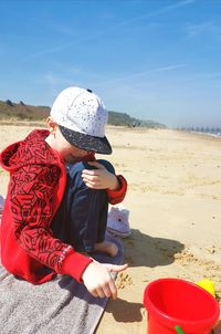 Full length of boy sitting on beach against sky
