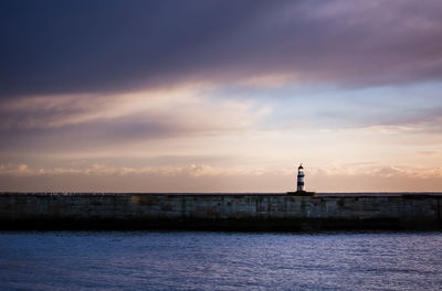 Lighthouse by sea against cloudy sky during sunset