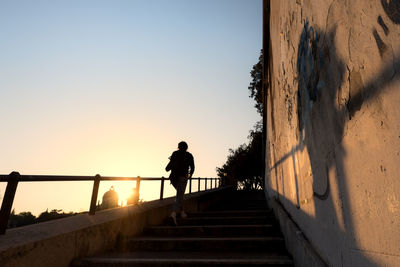 Silhouette woman walking on steps against sky during sunset