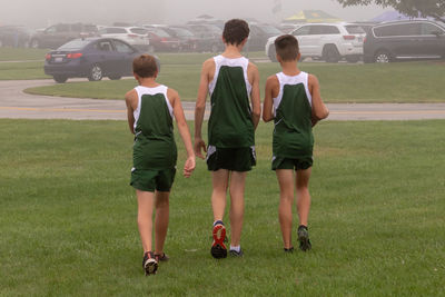 Rear view of male friends walking on grassy field towards cars