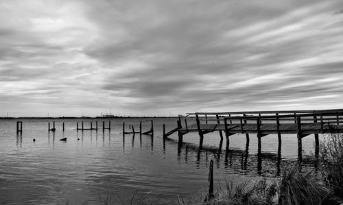 Wooden posts in lake against sky