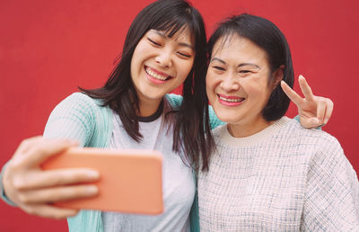 Smiling young woman taking selfie with mother while standing against red background