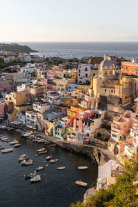 From above of picturesque scenery of costal town with colorful residential buildings located on procida island among sea with moored boats in sunny day