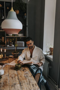 Man reading newspaper while sitting near table at home