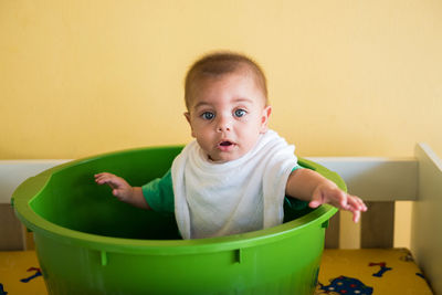 Portrait of cute baby boy sitting in bucket at home