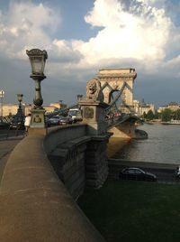 Statue of bridge over river against cloudy sky