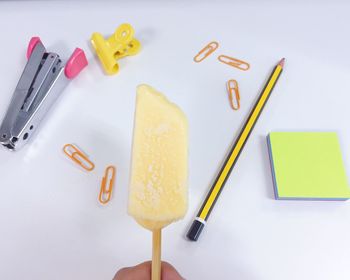 Cropped image of hand holding ice cream against office supplies on white background