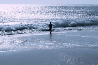 Rear view of man with surfboard standing on sea shore