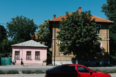 Red car on street against buildings during sunny day