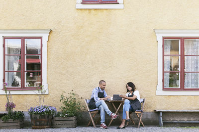 Man and woman discussing over digital tablet while sitting at table outside cafe