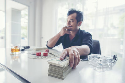 Thoughtful businessman with money and dices at desk in office