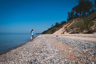 Man walking on shore against clear blue sky