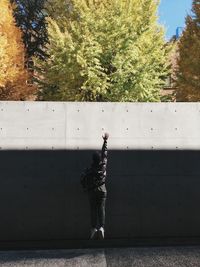 Rear view of man standing on footpath against wall