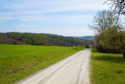 Empty road amidst field against sky