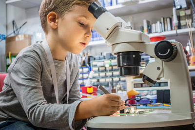 Side view of boy repairing computer chip on table