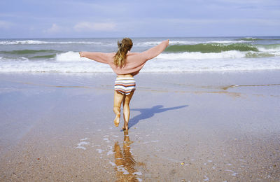 Teenage girl running on beach toward ocean