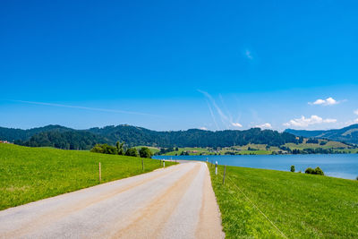 Road leading towards mountains against blue sky