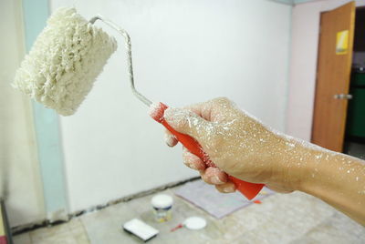 Cropped image of person holding paint roller at home