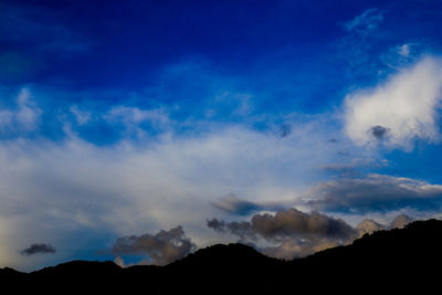 Low angle view of silhouette mountains against blue sky