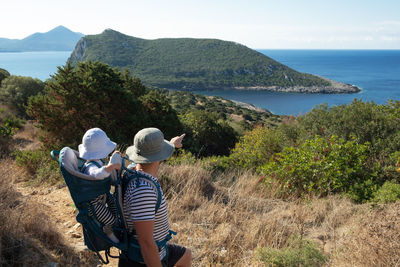 Man pointing at beach and mountains travelling with his daughter ,girl in baby carrier 