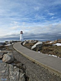 Pathway leading to lighthouse against clouds