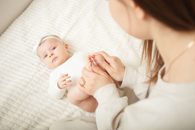 Mother massages her little daughter, newborn baby. lies on bed in bedroom, homely. legs, fingers.