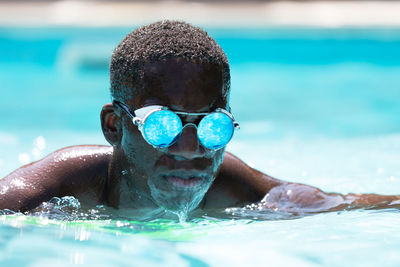 Calm african american male in stylish sunglasses with reflection of water swimming in pool against blurred background on sunny summer day