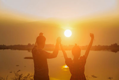 Silhouette people against orange sky during sunset