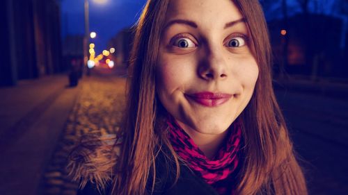 Close-up portrait of teenage girl smiling while standing on street at night