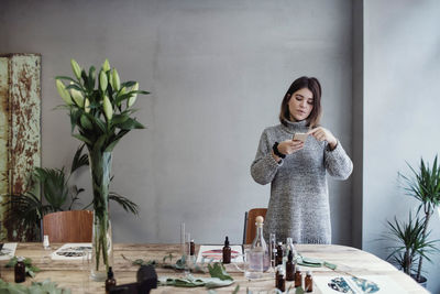 Mid adult female owner photographing various bottles on table at perfume workshop