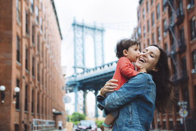 Usa, new york, new york city, baby kissing mother in brooklyn with manhattan bridge in the background