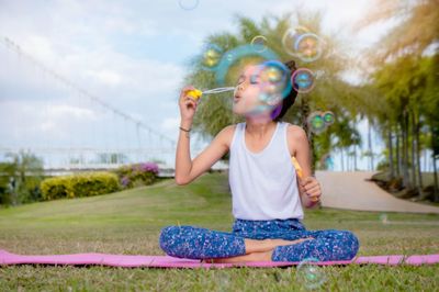 Full length of girl blowing bubbles on field