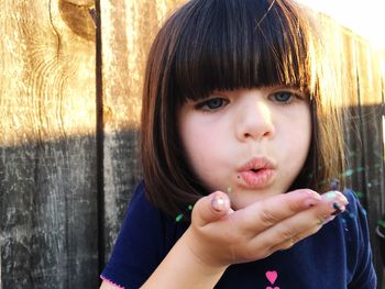 Close-up of girl blowing against wooden fence