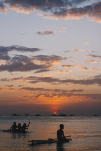 Silhouette people on sea against sky during sunset