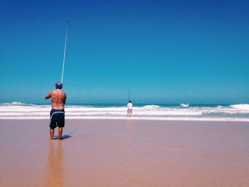 Rear view of men fishing at calm sea