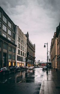 Wet street by buildings in city against sky