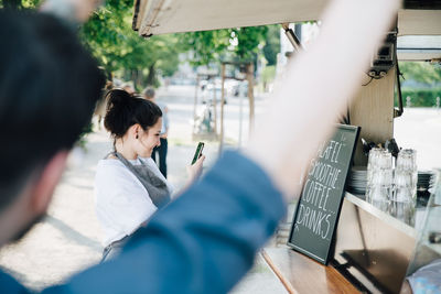 Female owner photographing board through smart phone while standing by food truck