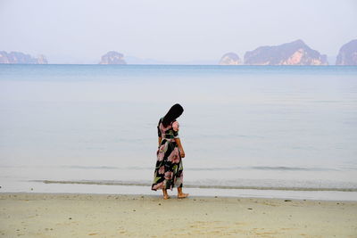 Woman walking at beach against sky