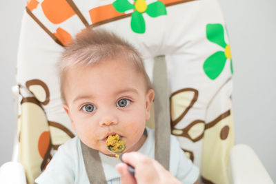 Cropped hand of person feeding food to cute boy at home